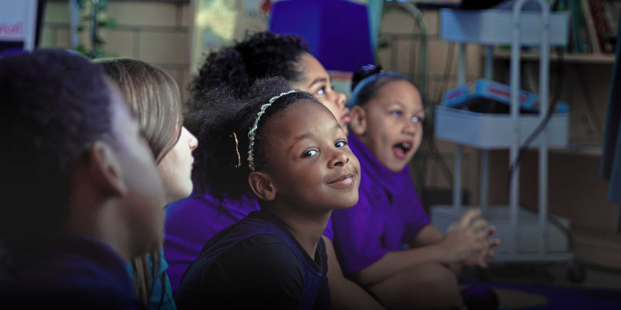 Smiling student sitting with classmates in purple shirts in a classroom.