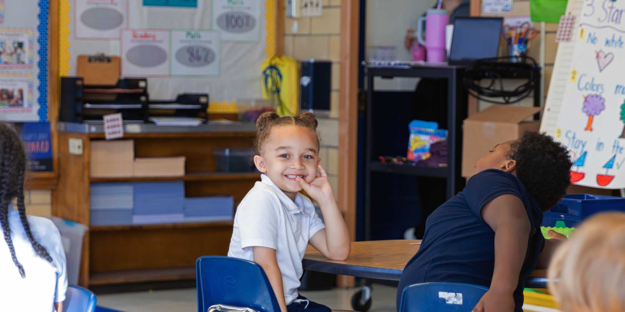 Young student smiling at a table in a classroom.