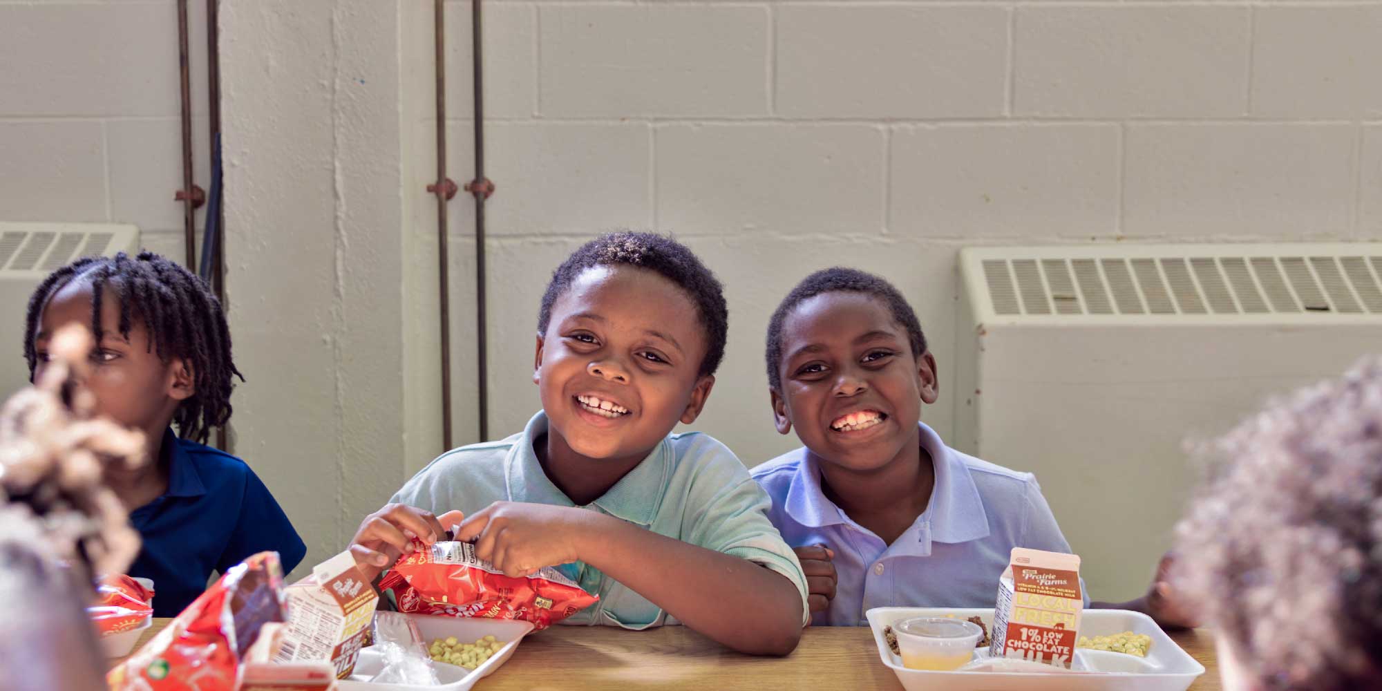 Two students smiling at a lunch table with meal trays.