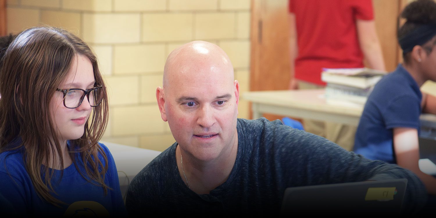 Teacher helping a student at a desk.